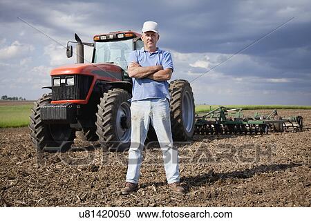 Stock Image - USA, Illinois, Metamora, mature farer standing in front of tractor on field. Fotosearch