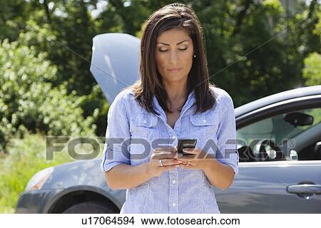 Picture - USA, Illinois, Metamora, mature woman text messaging in front of broken car. Fotosearch