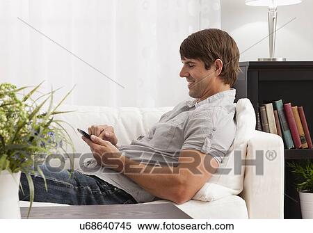 Stock Photography - USA, Illinois, Metamora, mid adult man sitting in living room and reading Digital Tablet. Fotosearch