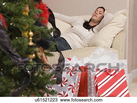 Stock Image - USA, Illinois, Metamora, mid adult woman reclining on sofa behind Christmas tree. Fotosearch
