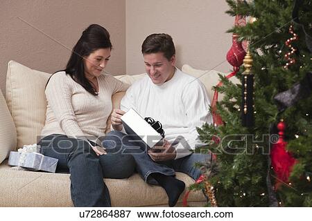 Stock Photo - USA, Illinois, Metamora, mid adult couple opening Christmas presents. Fotosearch