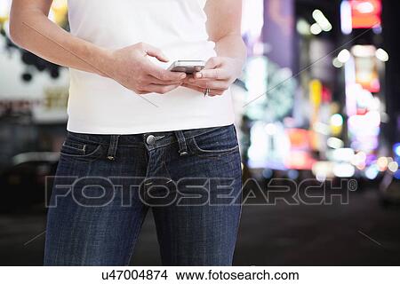 Picture - USA, Illinois, Metamora, Midsection of woman text-messaging in street at night. Fotosearch