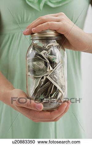 Stock Image - USA, Illinois, Metamora, Midsection of woman holding jar with money. Fotosearch