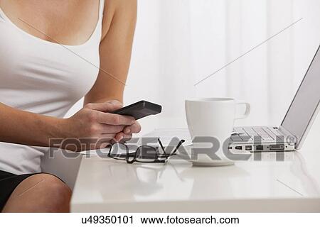 Stock Image - USA, Illinois, Metamora, Midsection of woman using cell phone and laptop. Fotosearch