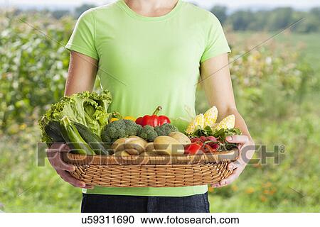Stock Image - USA, Illinois, Metamora, midsection of woman holding freshly harvested vegetables. Fotosearch