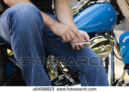 Stock Image - USA, Illinois, Metamora, midsection of man sitting on bike and texting on phone. Fotosearch