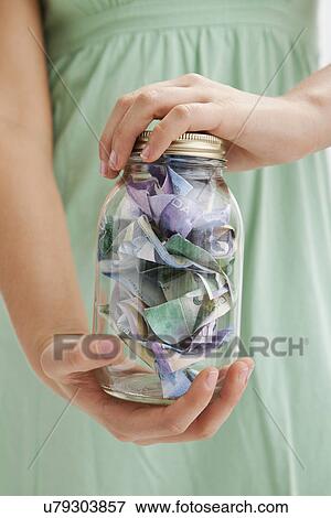 Stock Photo - USA, Illinois, Metamora, Midsection of woman holding jar with money. Fotosearch