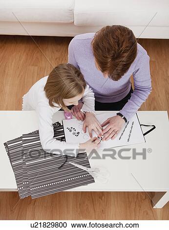 Stock Image - USA, Illinois, Metamora, Mother and daughter (8-9) making photo album at table. Fotosearch