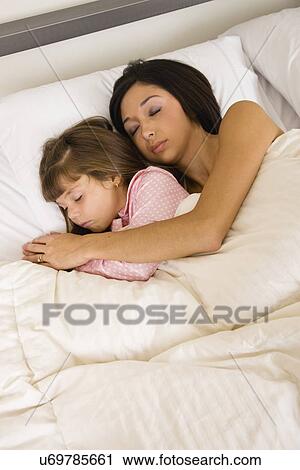 Stock Image - USA, Illinois, Metamora, Mother and daughter (6-7) asleep in bed. Fotosearch