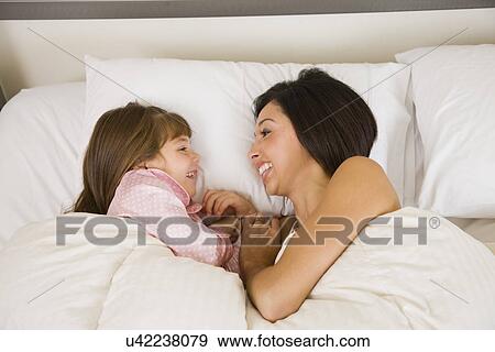 Stock Photo - USA, Illinois, Metamora, Mother and daughter (6-7) lying in bed. Fotosearch