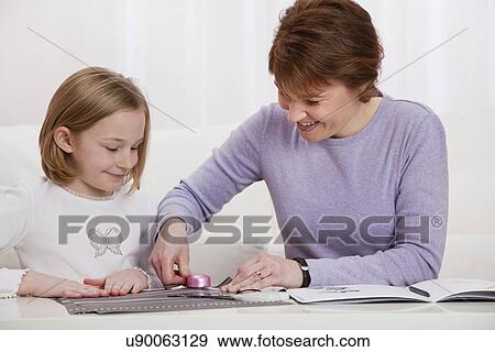 Stock Photo - USA, Illinois, Metamora, Mother and daughter (8-9) making photo album at table. Fotosearch