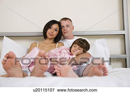 Stock Photo - USA, Illinois, Metamora, Parents with daughter (6-7) sleeping on bed. Fotosearch
