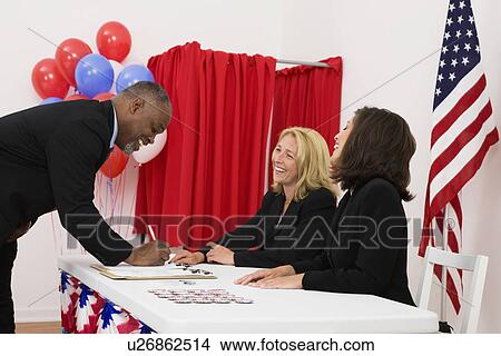 Picture - USA, Illinois, Metamora, People at polling place table, US flag, balloons and voting booth in background. Fotosearch