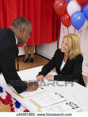 Stock Photography - USA, Illinois, Metamora, People at polling place table, balloons and voting booth in background. Fotosearch
