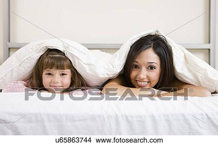 Picture - USA, Illinois, Metamora, Portrait of mother and daughter (6-7) lying in bed. Fotosearch