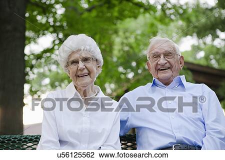 Stock Image - USA, Illinois, Metamora, Portrait of senior couple in sitting on bench park. Fotosearch