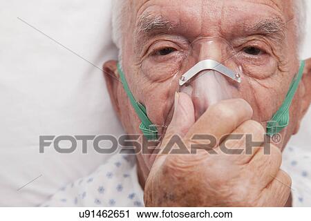 Stock Image - USA, Illinois, Metamora, Portrait of senior man with oxygen mask lying in hospital bed. Fotosearch