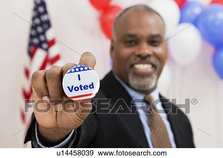 USA, Illinois, Metamora, Portrait of smiling man holding vote button, US flag and balloons in background View Large Photo Image Stock Photo - USA, Illinois, Metamora, Portrait of smiling man holding vote button, US flag and balloons in background. Fotosearch