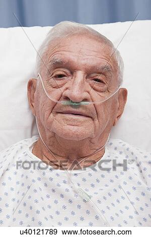 Stock Photo - USA, Illinois, Metamora, Portrait of senior man with ear nasal cannula lying in hospital bed. Fotosearch
