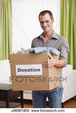 Stock Photography - USA, Illinois, Metamora, Portrait of smiling man carrying cardboard box with clothes. Fotosearch