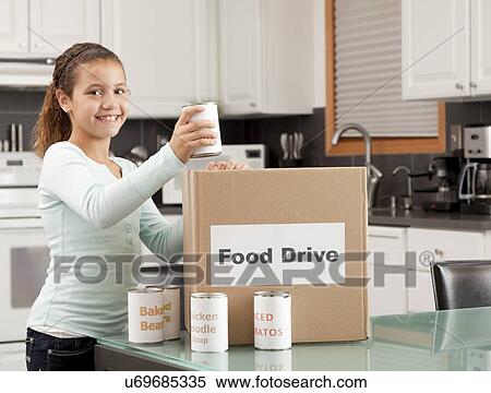 Stock Photography - USA, Illinois, Metamora, Portrait of smiling girl (10-11) putting canned food into cardboard box in kitchen. Fotosearch