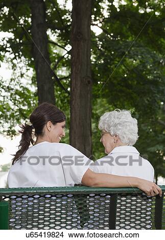 USA, Illinois, Metamora, Rear view of female nurse and senior woman sitting on park bench View Large Photo Image Picture - USA, Illinois, Metamora, Rear view of female nurse and senior woman sitting on park bench. Fotosearch