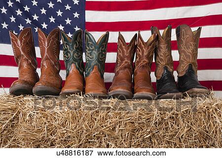 Stock Photo - USA, Illinois, Metamora, Row of cowboy boots on haystack with American flag on background. Fotosearch