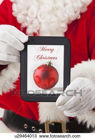 Stock Image - USA, Illinois, Metamora, Santa claus holding digital tablet with christmas decoration on screen. Fotosearch