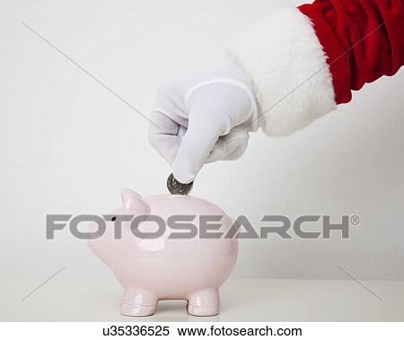 Stock Photography - USA, Illinois, Metamora, Santa claus putting coin into piggy bank. Fotosearch