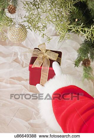 Stock Photo - USA, Illinois, Metamora, Santa clause putting gift under Christmas tree. Fotosearch