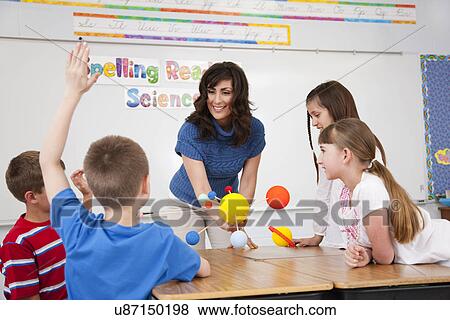 Stock Photo - USA, Illinois, Metamora, Schoolchildren (8-9, 10-11) and female teacher with solar system model at science class. Fotosearch
