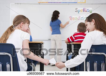 USA, Illinois, Metamora, Schoolgirls (8-9, 10-11) passing letter in classroom, female teacher at whiteboard in background View Large Photo Image Stock Photo - USA, Illinois, Metamora, Schoolgirls (8-9, 10-11) passing letter in classroom, female teacher at whiteboard in background. Fotosearch