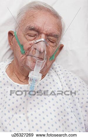 Stock Photo - USA, Illinois, Metamora, Senior man with oxygen mask sleeping in hospital bed. Fotosearch
