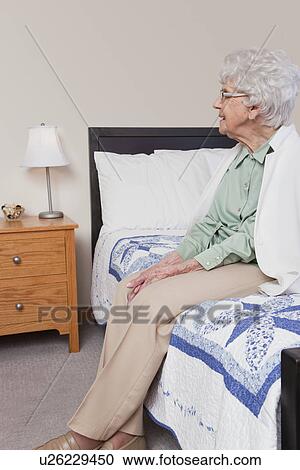 Stock Image - USA, Illinois, Metamora, Senior woman sitting on bed. Fotosearch