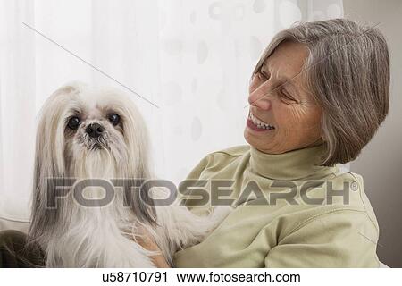 Stock Image - USA, Illinois, Metamora, Senior woman sitting on sofa with dog. Fotosearch