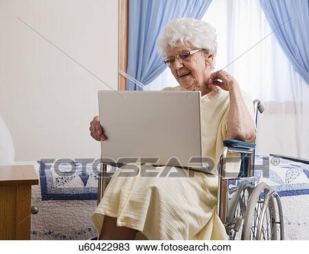 Stock Image - USA, Illinois, Metamora, Senior woman on wheelchair using laptop. Fotosearch