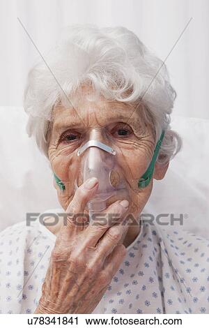 Stock Image - USA, Illinois, Metamora, Senior woman with oxygen mask lying in hospital bed. Fotosearch