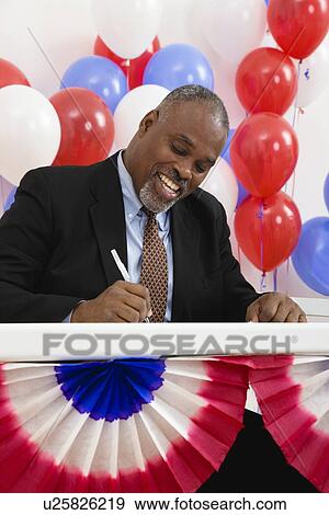 USA, Illinois, Metamora, Smiling man writing at polling place table, balloons in background View Large Photo Image Stock Photo - USA, Illinois, Metamora, Smiling man writing at polling place table, balloons in background. Fotosearch
