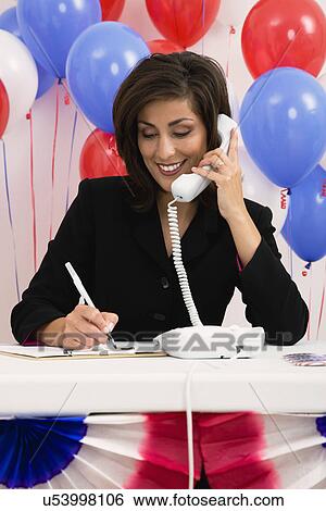 Stock Photograph - USA, Illinois, Metamora, Smiling woman talking on phone, red and blue balloons in background. Fotosearch