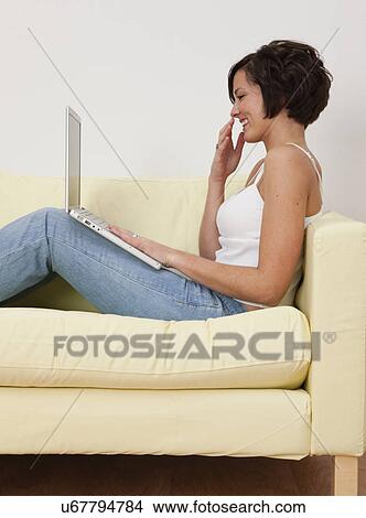 USA, Illinois, Metamora, Smiling young woman sitting on sofa with laptop View Large Photo Image Picture - USA, Illinois, Metamora, Smiling young woman sitting on sofa with laptop. Fotosearch