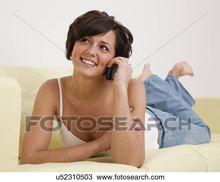 Stock Image - USA, Illinois, Metamora, Smiling young woman lying on sofa and talking on mobile phone. Fotosearch