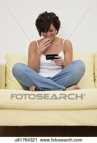 USA, Illinois, Metamora, Smiling young woman sitting on sofa with smart phone View Large Photo Image Stock Image - USA, Illinois, Metamora, Smiling young woman sitting on sofa with smart phone. Fotosearch
