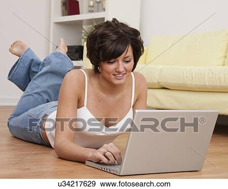 USA, Illinois, Metamora, Smiling young woman lying on floor with laptop View Large Photo Image Stock Photo - USA, Illinois, Metamora, Smiling young woman lying on floor with laptop. Fotosearch