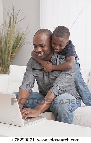 Stock Image - USA, Illinois, Metamora, Son (6-7) embracing father on sofa. Fotosearch