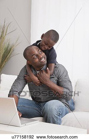 Stock Image - USA, Illinois, Metamora, Son (6-7) embracing father on sofa. Fotosearch