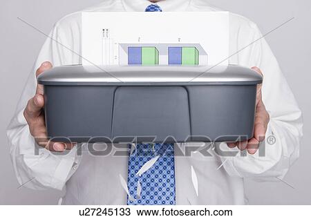Stock Image - USA, Illinois, Metamora, Studio shot of man holding paper shredder, mid section. Fotosearch