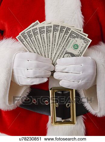 Stock Image - USA, Illinois, Metamora, Studio shot of Santa holding fan of one dollar banknotes, mid section. Fotosearch