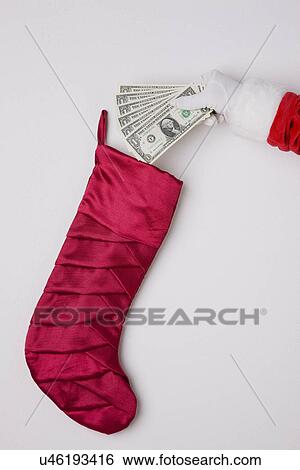 Stock Photograph - USA, Illinois, Metamora, Studio shot of Santa's hand putting fan of one dollar banknotes into Christmas stocking. Fotosearch