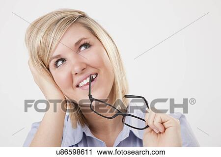 Stock Image - USA, Illinois, Metamora, studio portrait of young woman biting eyeglasses. Fotosearch