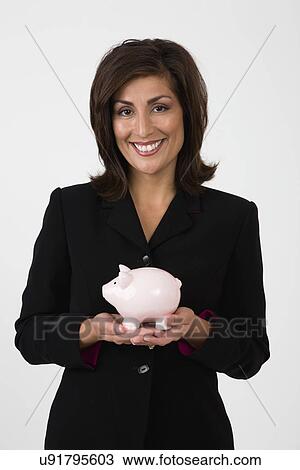 Stock Image - USA, Illinois, Metamora, Studio Portrait of smiling woman holding piggy bank. Fotosearch